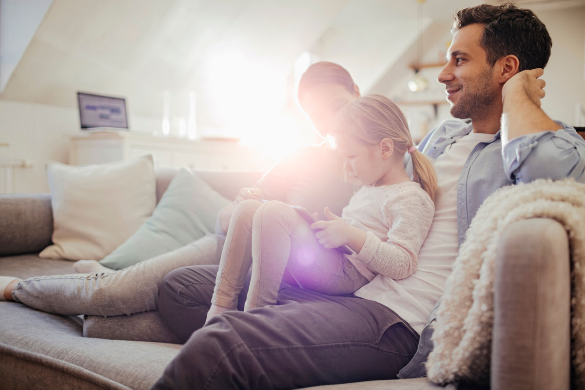 Mother and father sitting on a sofa together with their daughter using a tablet