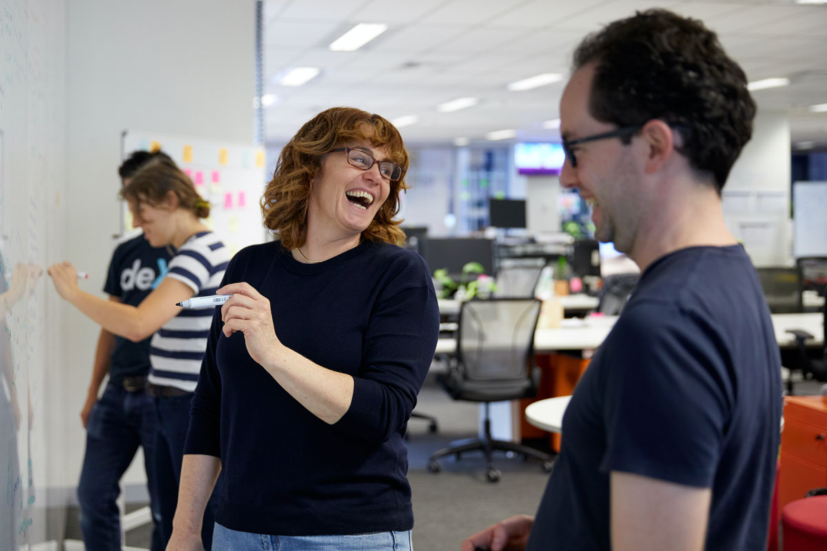 Four GreenSync team members writing on a whiteboard and laughing