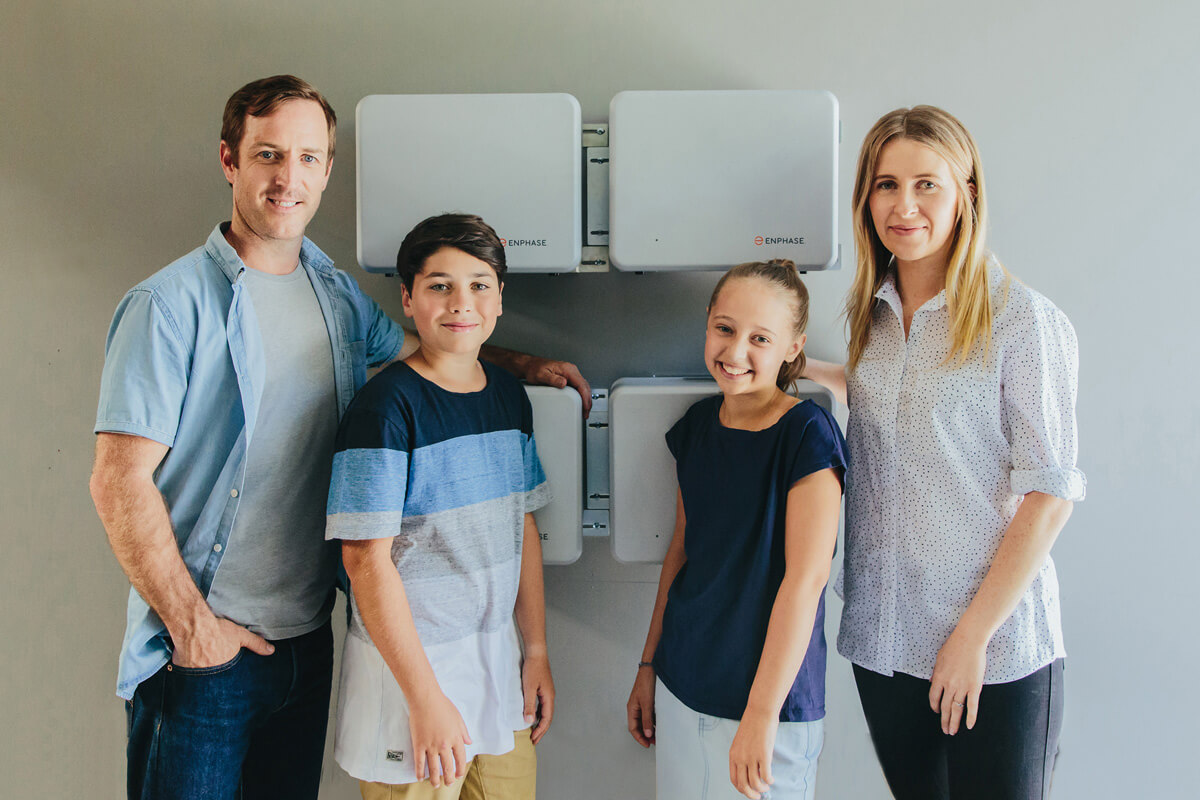 A family of four posing in front of their wall-mounted Enphase battery